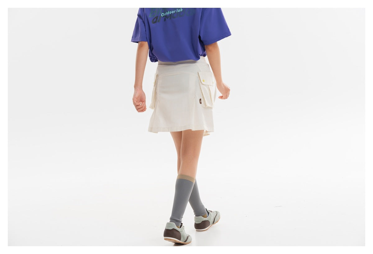 Rear view of a model wearing an ivory utility skort with a flap cargo pocket and a purple T-shirt.