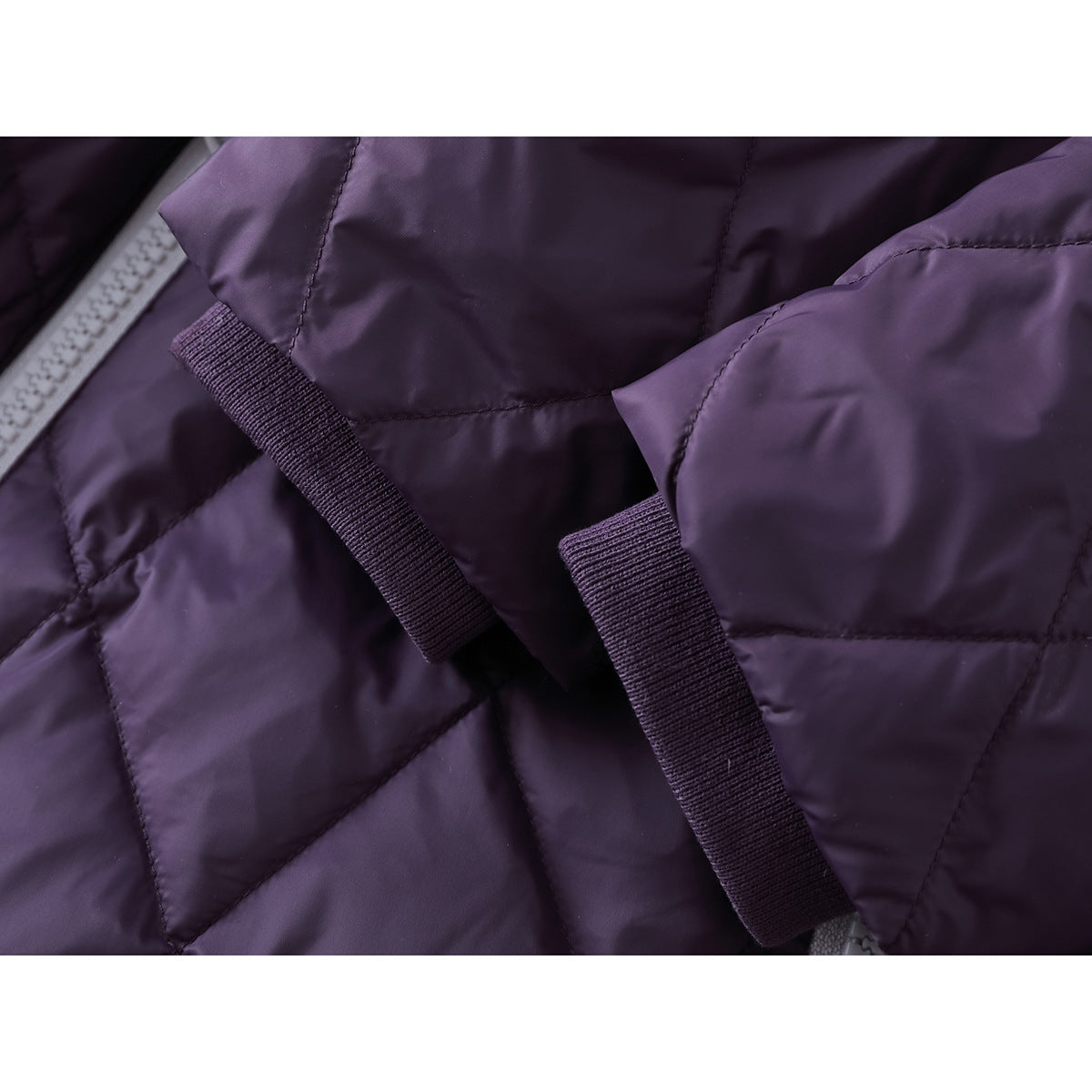 Close-up of purple quilted jacket fabric and two narrow matching fabric tabs beside the zipper.