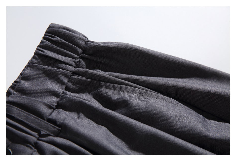 Close-up of dark charcoal trousers showing a gathered waistband and pleated fabric.