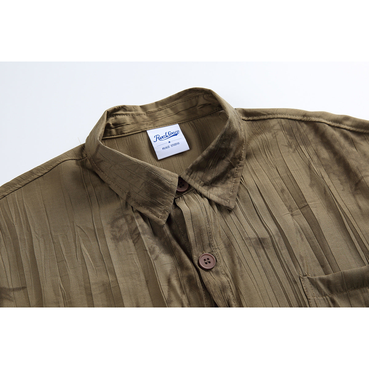 Close-up of an olive-brown shirt showing its pointed collar, brown buttons, textured pattern, and sewn-in label.