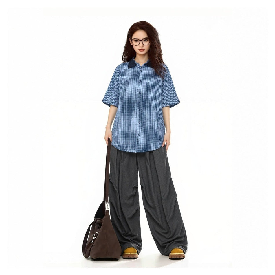 Model wearing a blue checked short-sleeve button-up shirt with a dark collar and charcoal wide-leg pants.