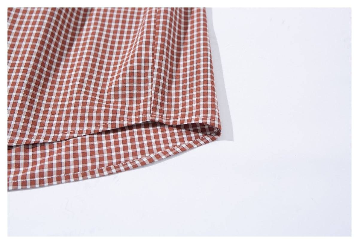 Close-up of the curved stitched hem on a rust-brown and white gingham shirt.