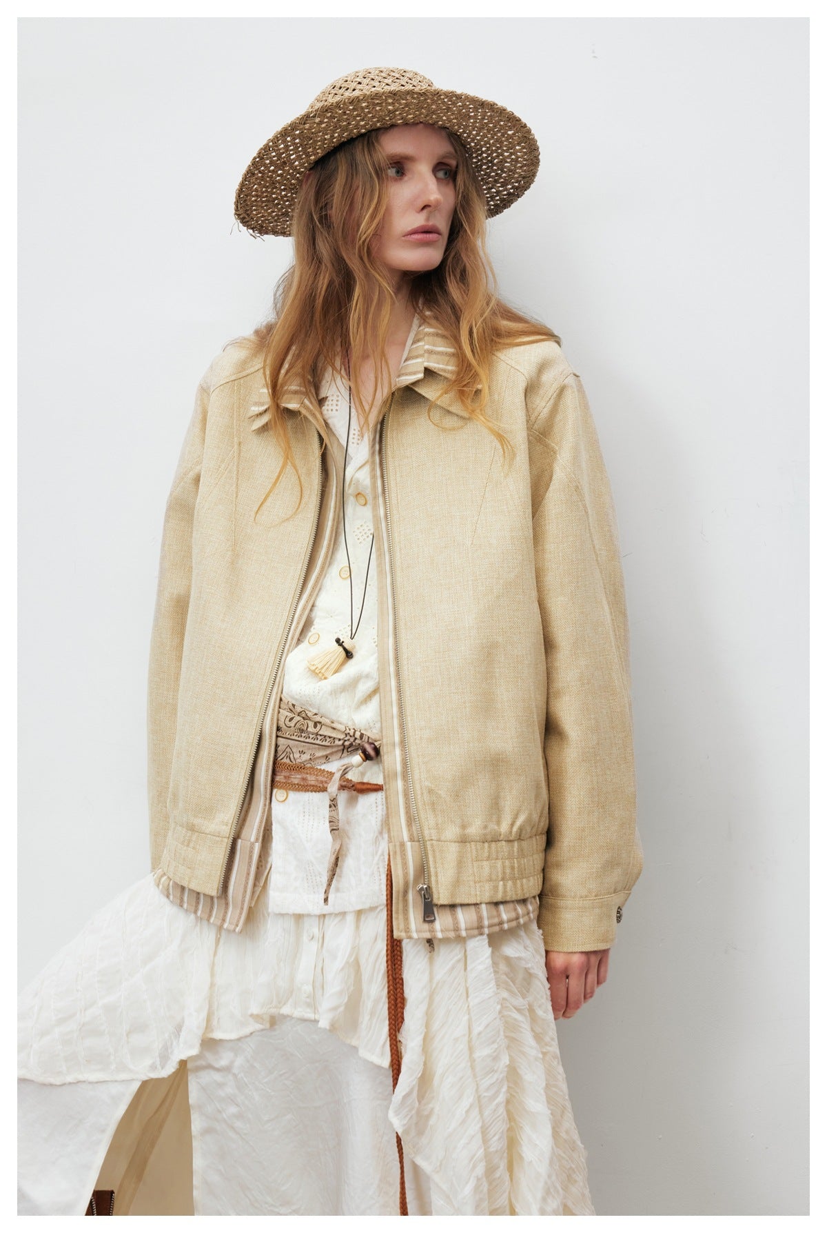 Close view of a model wearing a pale beige zip jacket with a striped collar over a white outfit.
