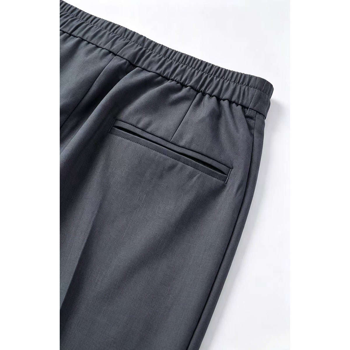 Close-up of charcoal-gray trousers showing an elasticated back waistband and a single welt pocket.