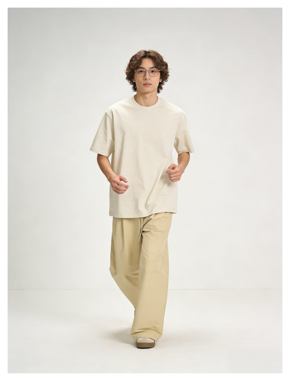 Model walking toward the camera in an off-white oversized T-shirt and light beige wide-leg pants.