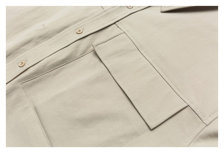 Close-up of a beige shirt's button placket and rectangular chest pocket with visible stitching.
