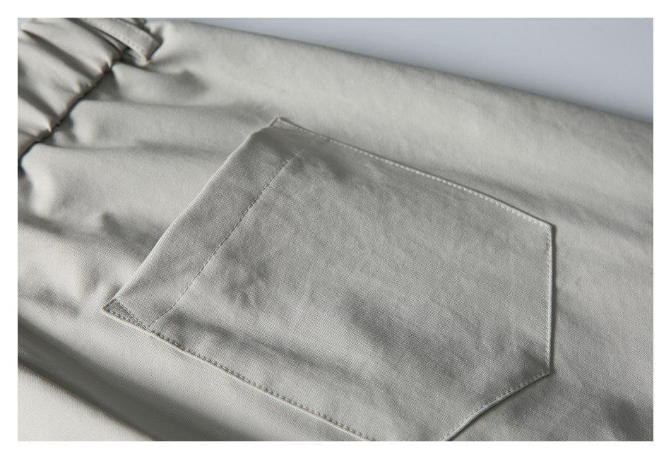 Close-up of a large stitched patch pocket on light gray trousers.
