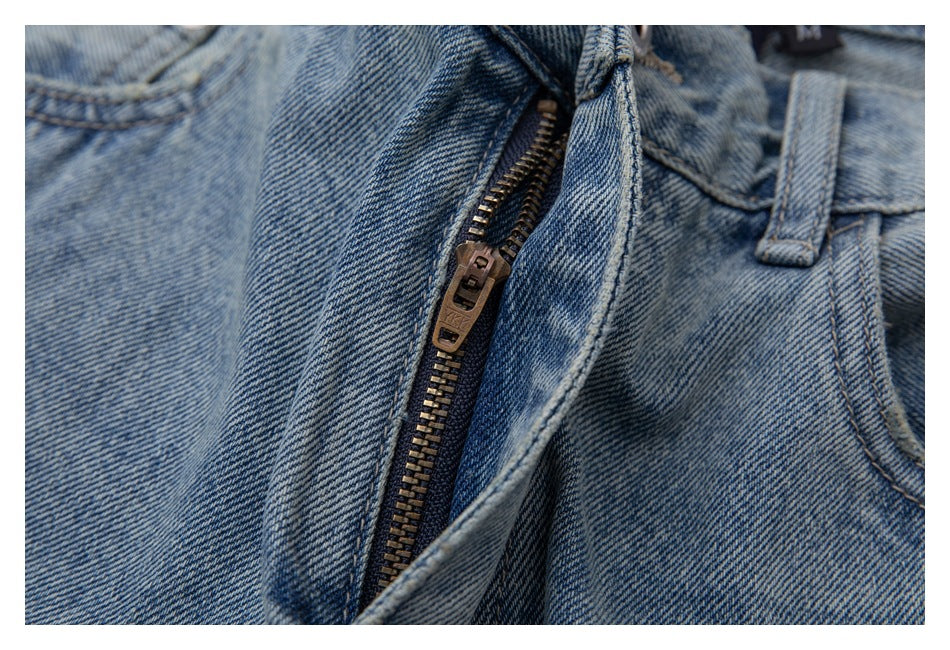 Close-up of light blue washed jeans with the zipper fly open, showing the metal zipper and stitching.
