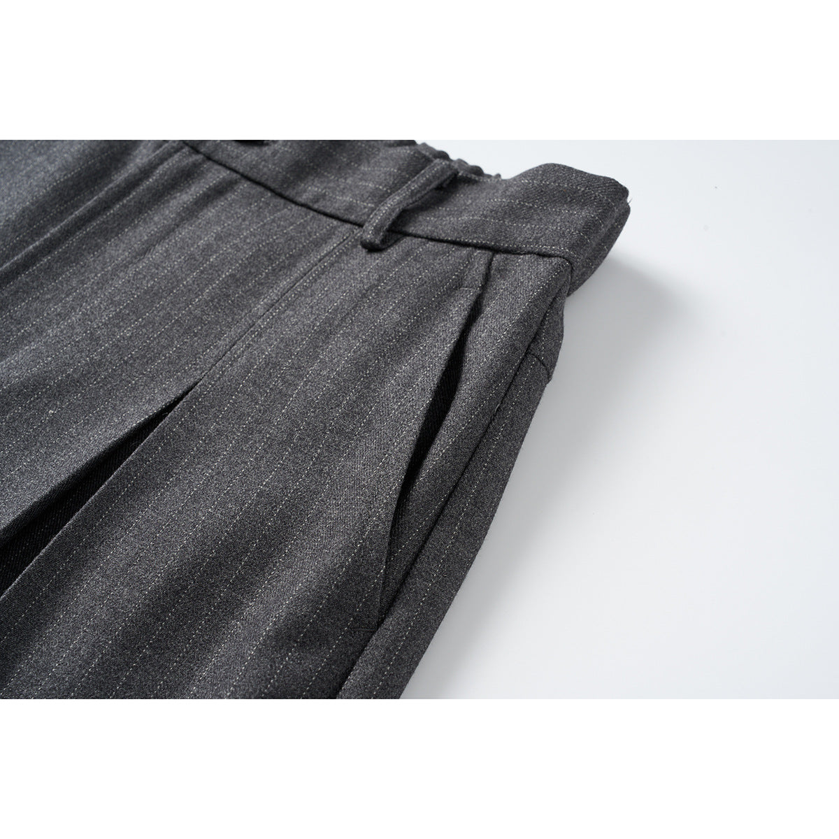 Close-up of dark charcoal pinstripe trousers showing a belt loop, pleat and side pocket opening.