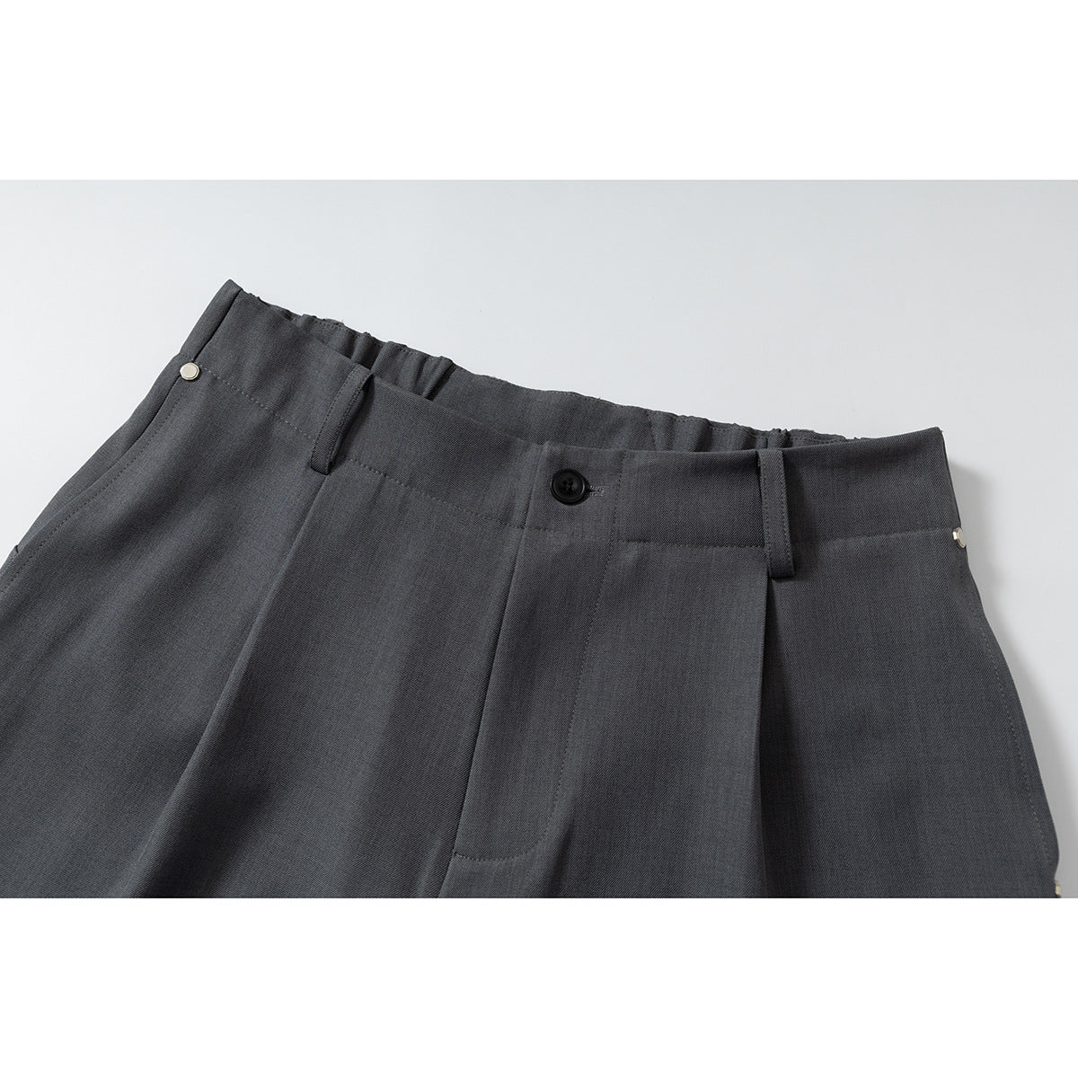 Close-up of charcoal gray wide-leg shorts showing the waistband, belt loops, button, pleats and front closure.