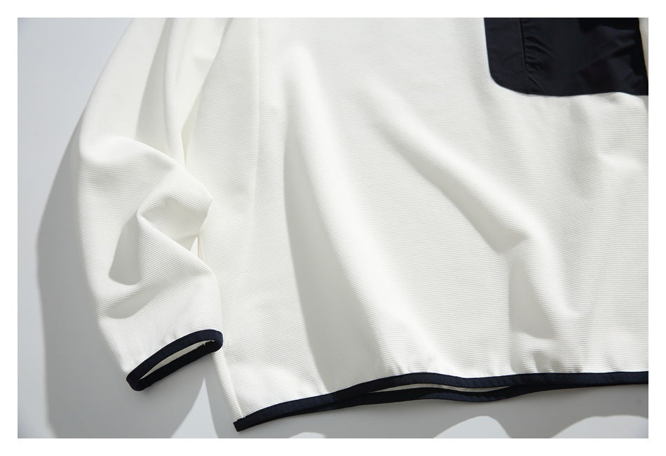 Close-up of a white ribbed shirt with black sleeve-cuff and hem trim; part of a black chest pocket is visible.