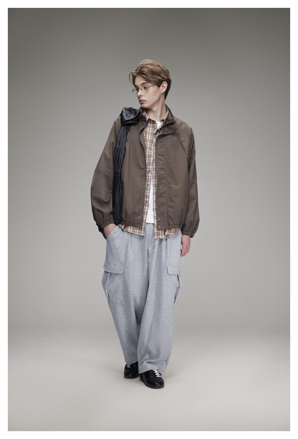 Model facing forward in a brown jacket with a stand collar, checked shirt, gray cargo pants, and black shoes.
