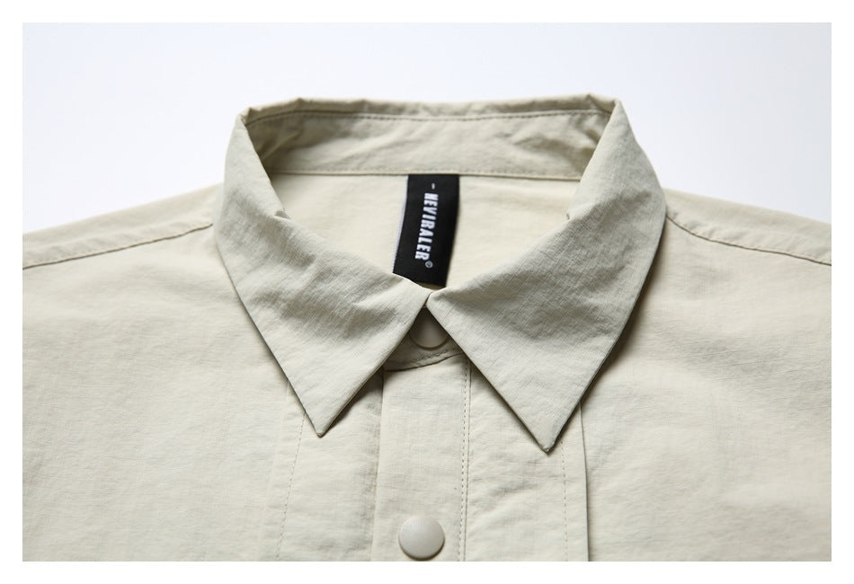 Close-up of the light beige shirt's pointed collar, front snap, and black neck label.