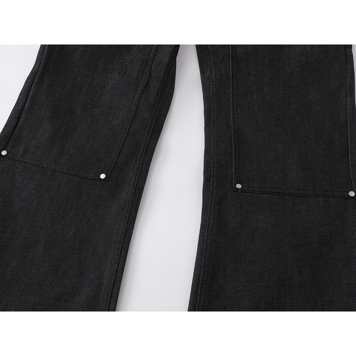 Close-up of black denim pant legs with large rectangular utility pockets and metal rivets.