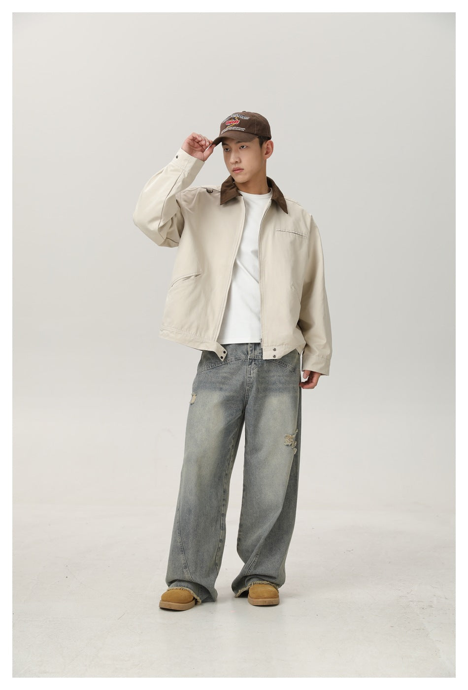Full-length front view of a model in a cream jacket with a brown collar, white shirt, and loose distressed jeans.