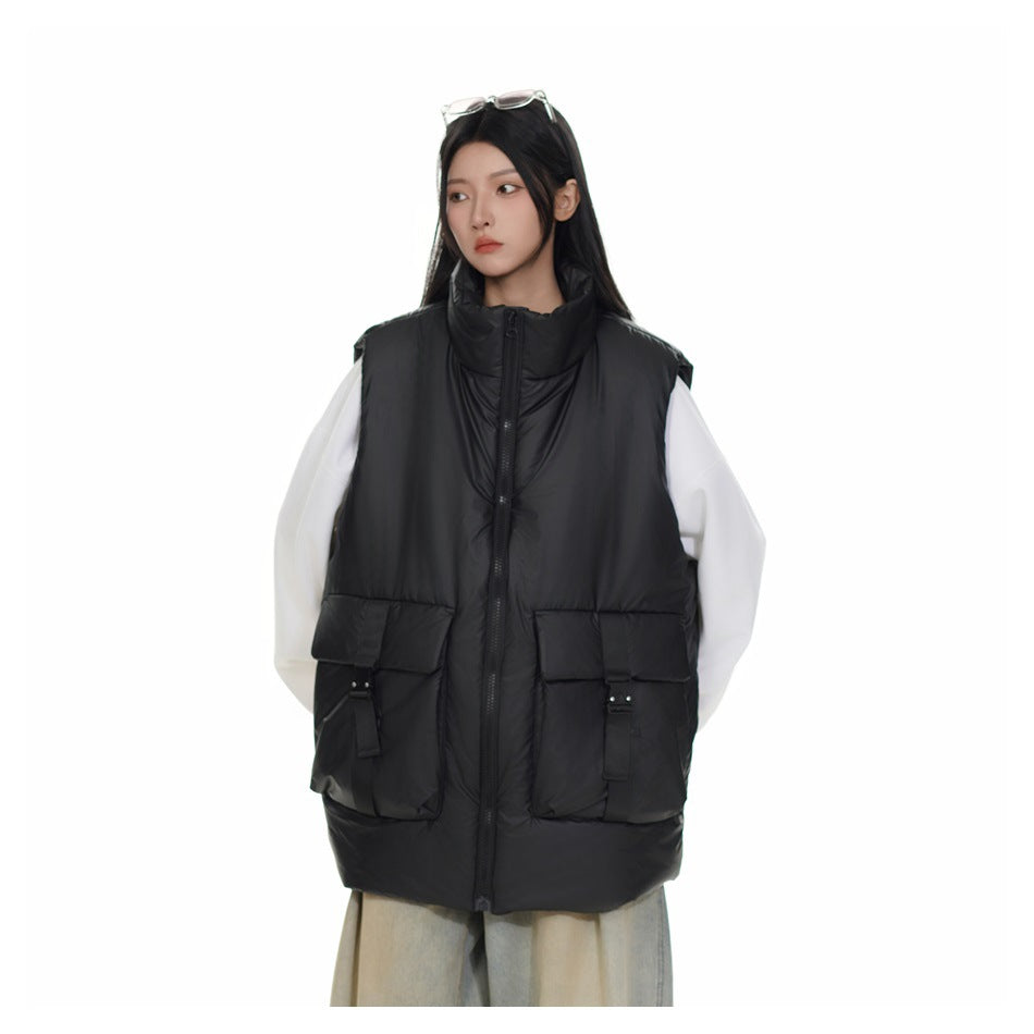 Model wearing a black padded high-collar vest with a front zip and oversized buckle-detail pockets over white sleeves.