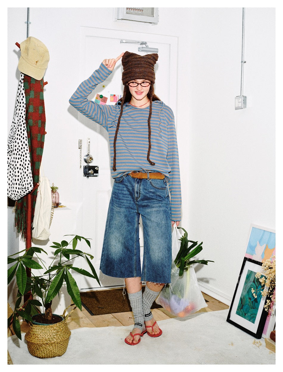 Model wearing a blue and taupe striped hooded top with wide-leg denim culottes, gray socks, and red sandals.