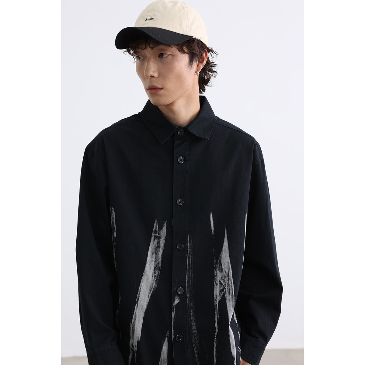 Close view of a model wearing a black button-up shirt with abstract white brushstroke graphics.
