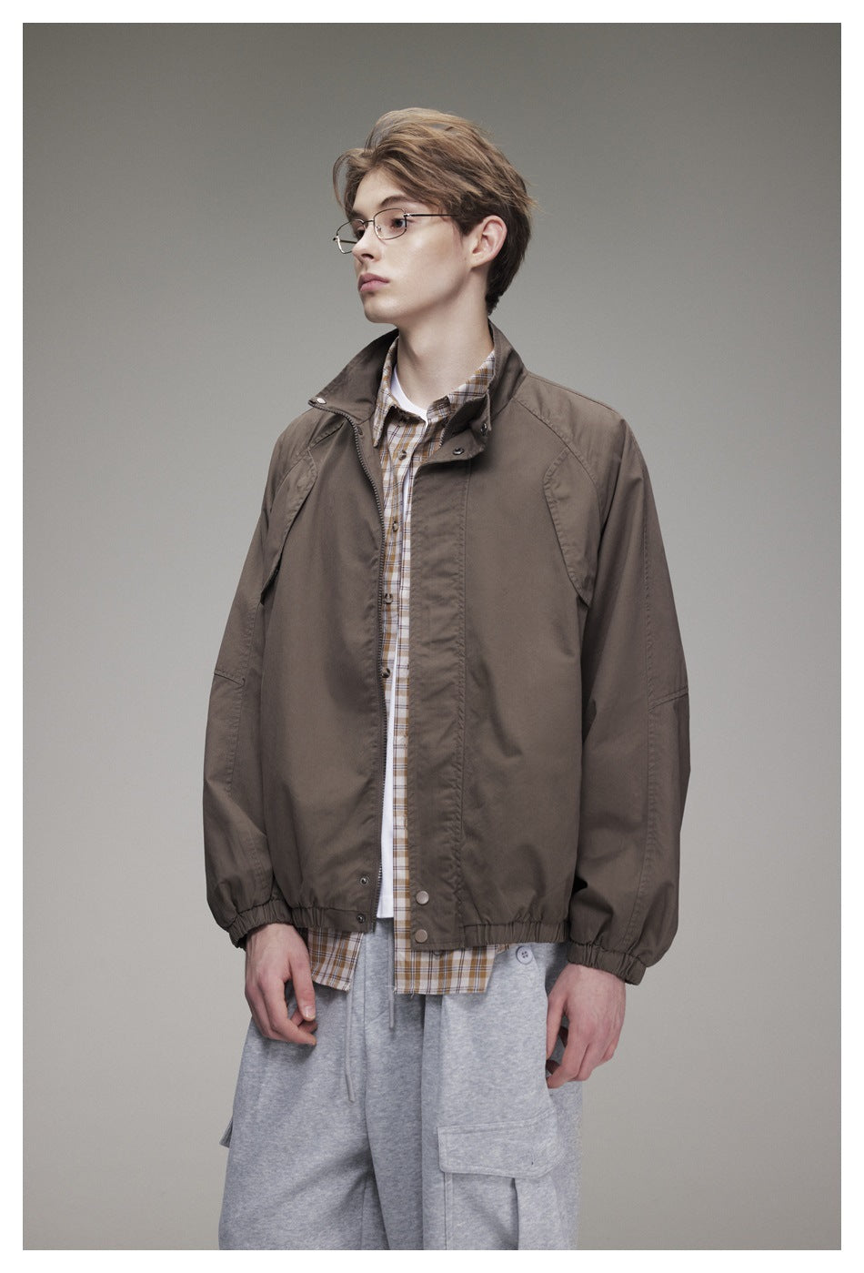 Model wearing a brown zip-front jacket over a checked shirt, with gray cargo pants.