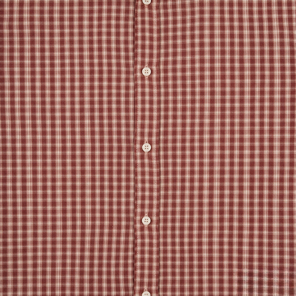 Close-up of rust-red and cream plaid shirt fabric with a button placket and white buttons.