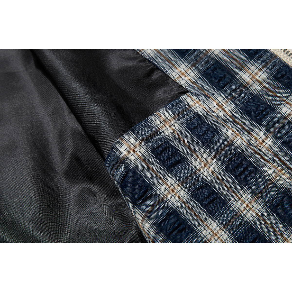 Close-up of dark fabric beside blue, cream, and tan plaid jacket lining.