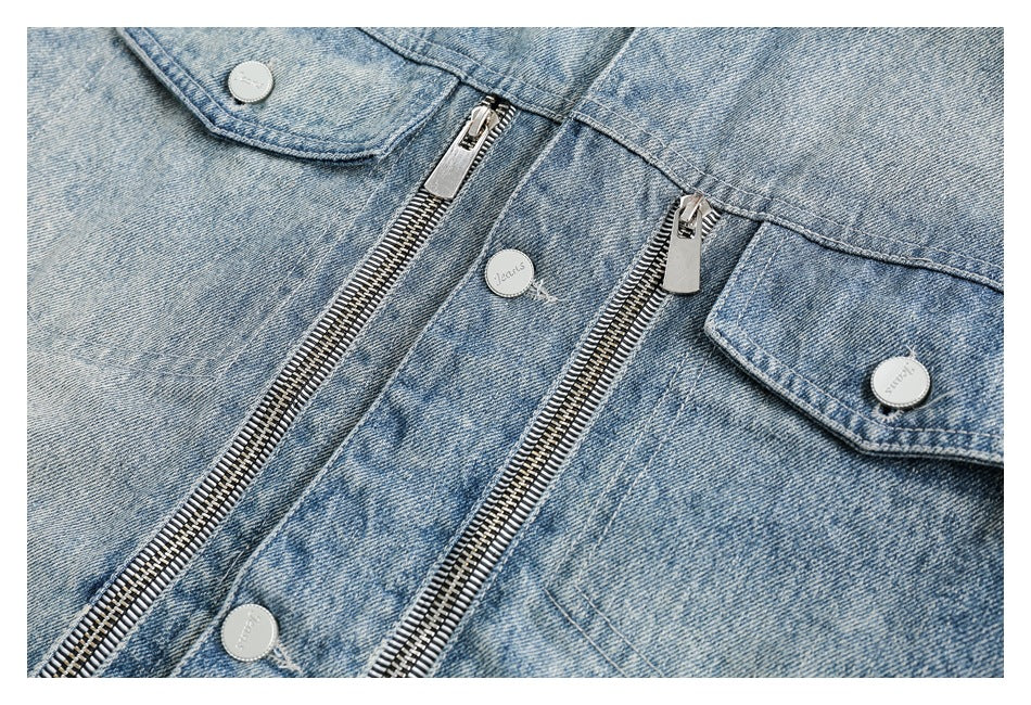 Close-up of a light blue denim jacket with two metal zippers, flap pockets, and silver buttons.