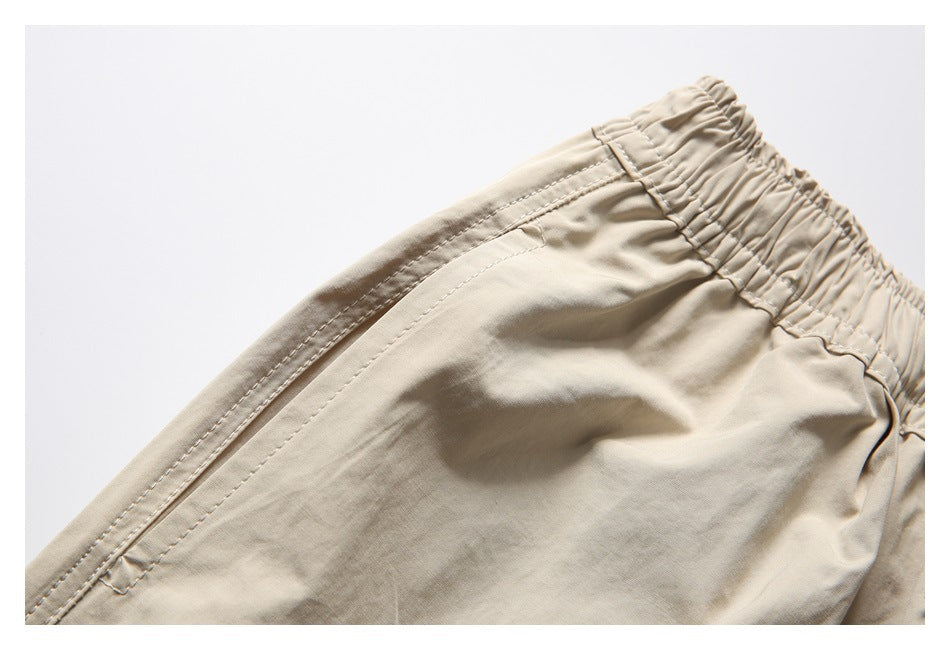 Close-up of beige trousers showing the elastic waistband and stitched pocket opening.