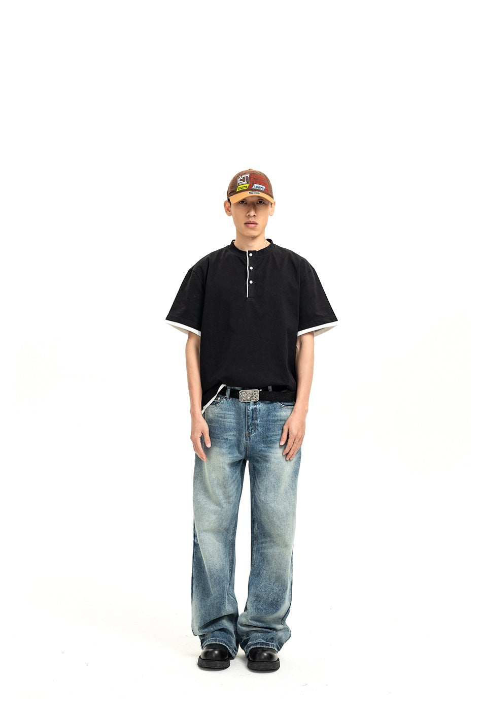 Front view of a model wearing a black short-sleeve Henley shirt with white sleeve trim and loose blue jeans.