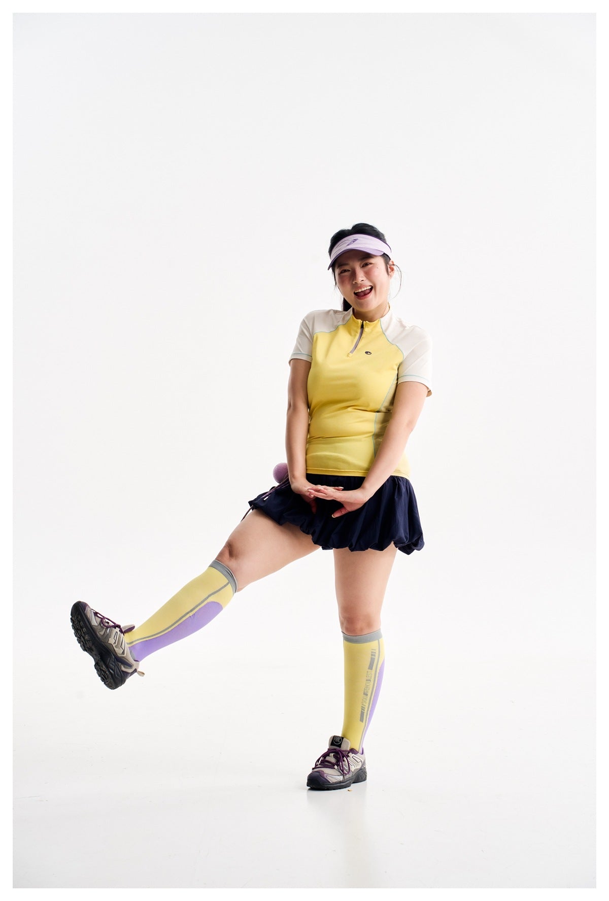 Model in a yellow and ivory zip-neck athletic top, navy bubble skirt, yellow socks and visor.