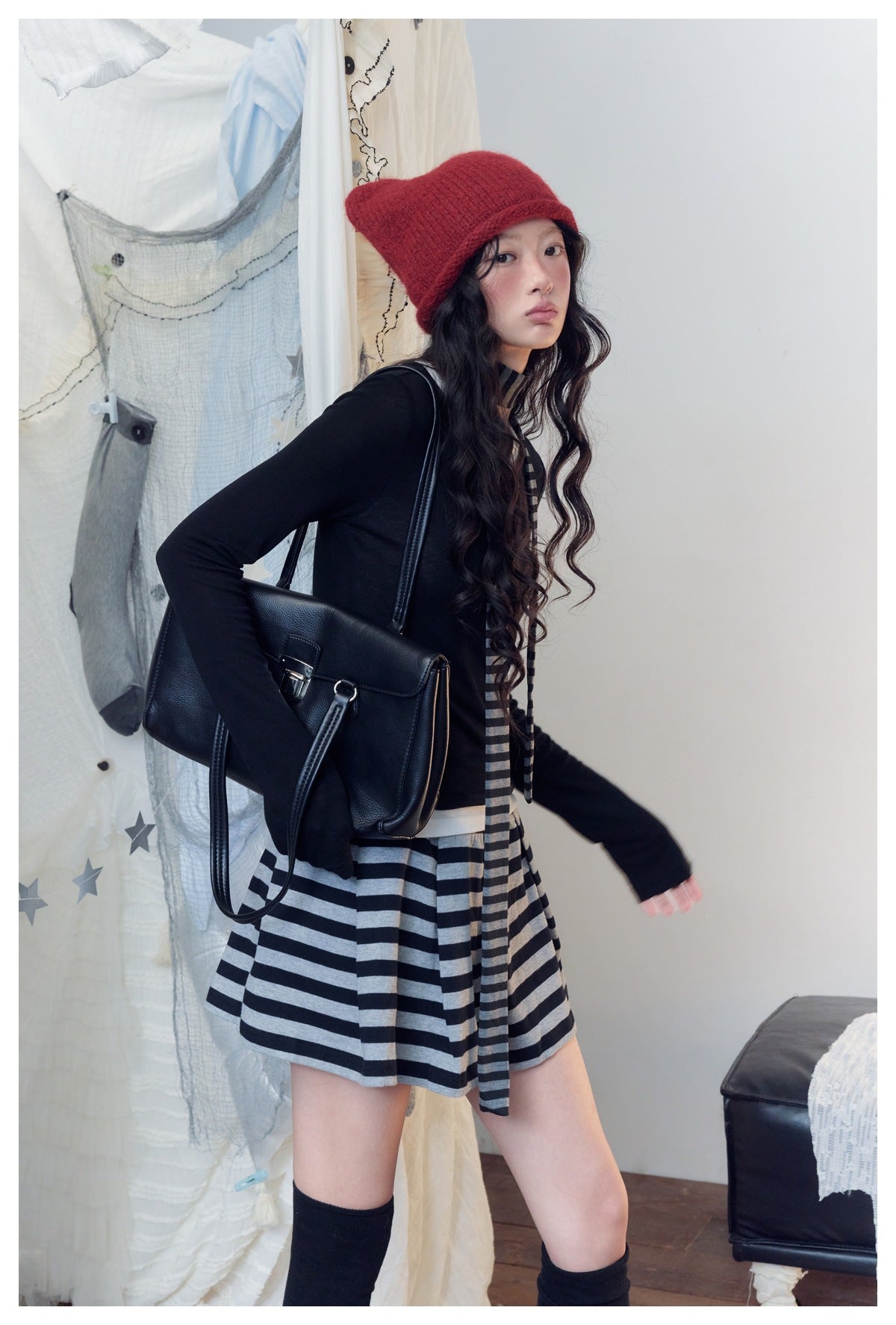 Model in a black long-sleeve top and striped mini skirt, with a matching scarf and red knit hat.