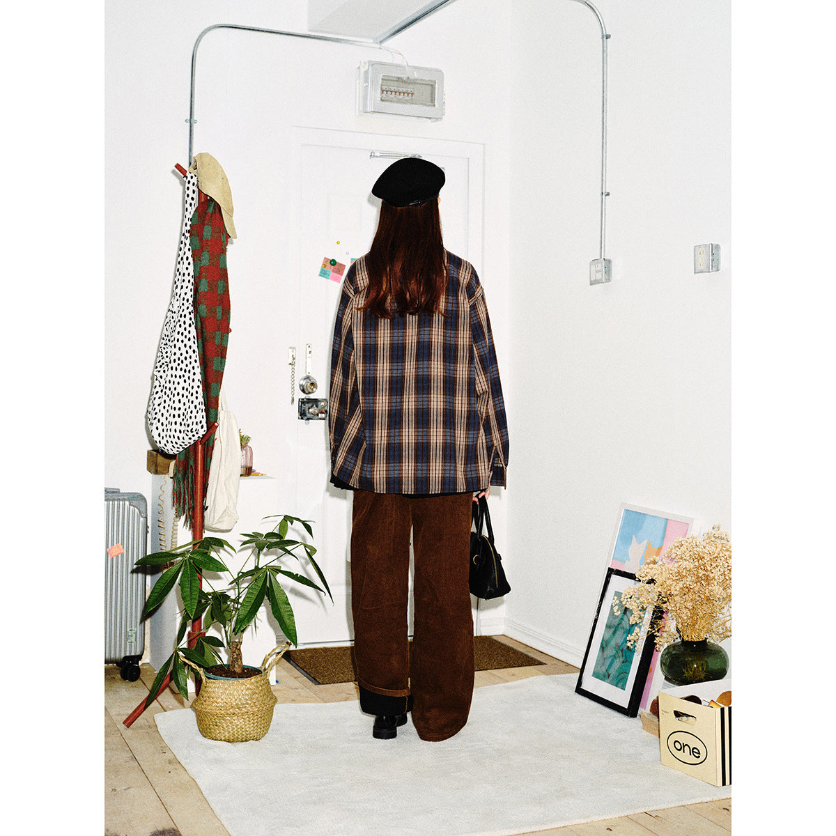 Back view of a model in a blue, brown and beige plaid shirt and loose brown pants.