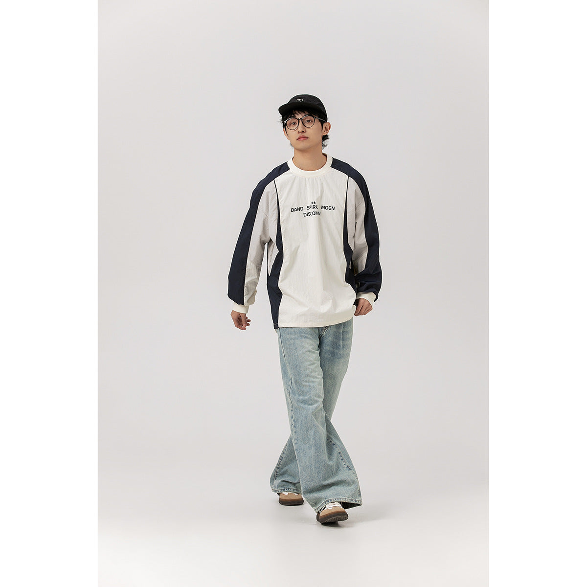 Model wearing an ivory and navy color-block long-sleeve pullover with chest lettering and light-wash wide-leg jeans.