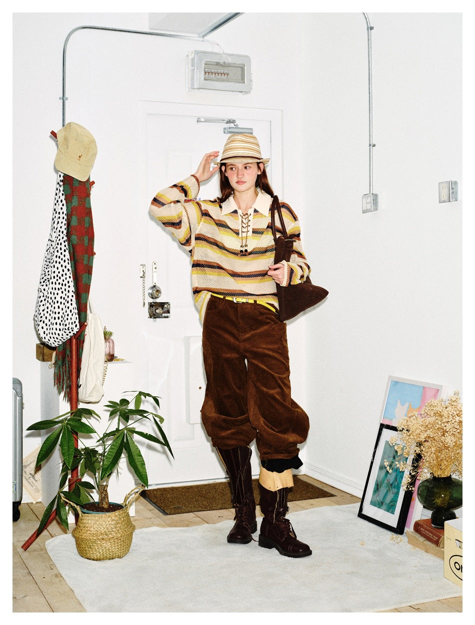 Full-length model wearing a cream open-knit sweater with yellow, brown, and navy stripes and a lace-up collar.