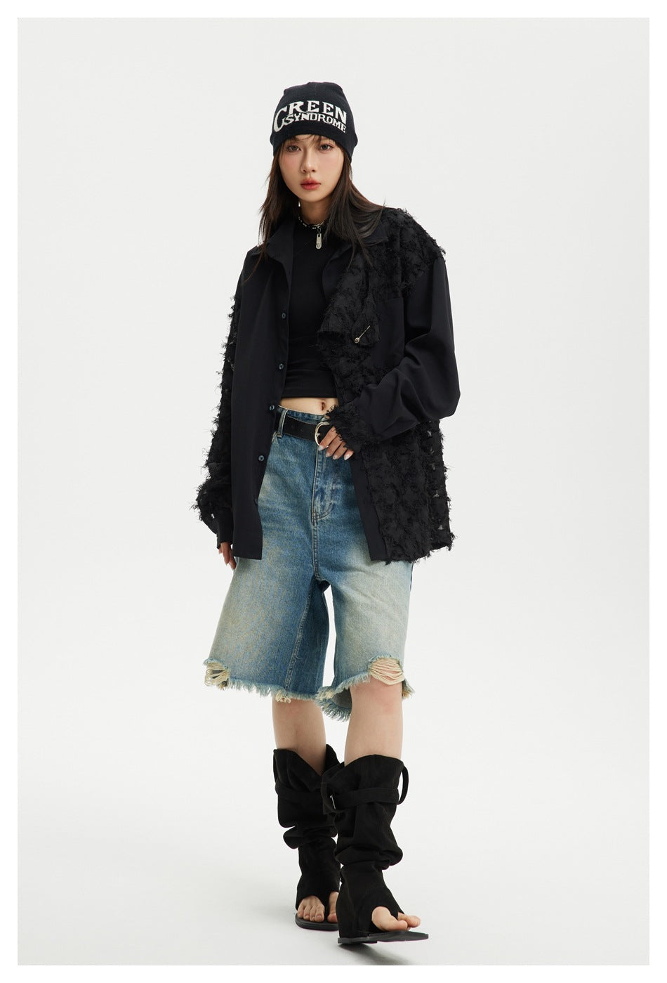 Model wearing the black fringe-panel shirt open over a black top with distressed denim shorts and black boots