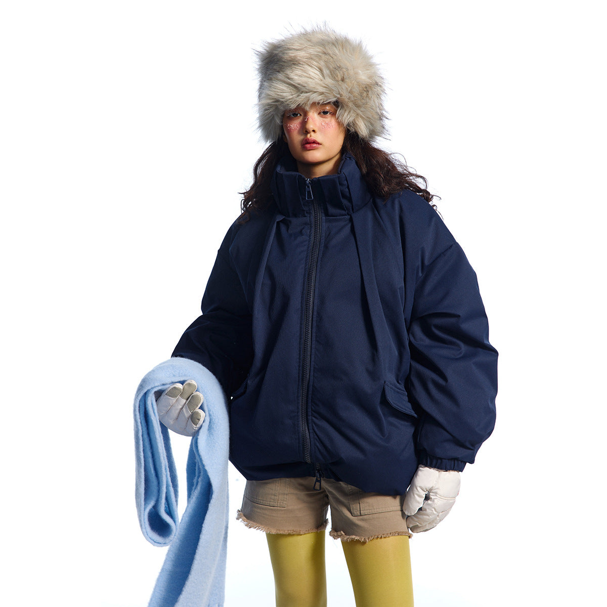 Model wearing a navy oversized zip jacket with a high collar and flap pockets, paired with a furry hat, gloves, and scarf.
