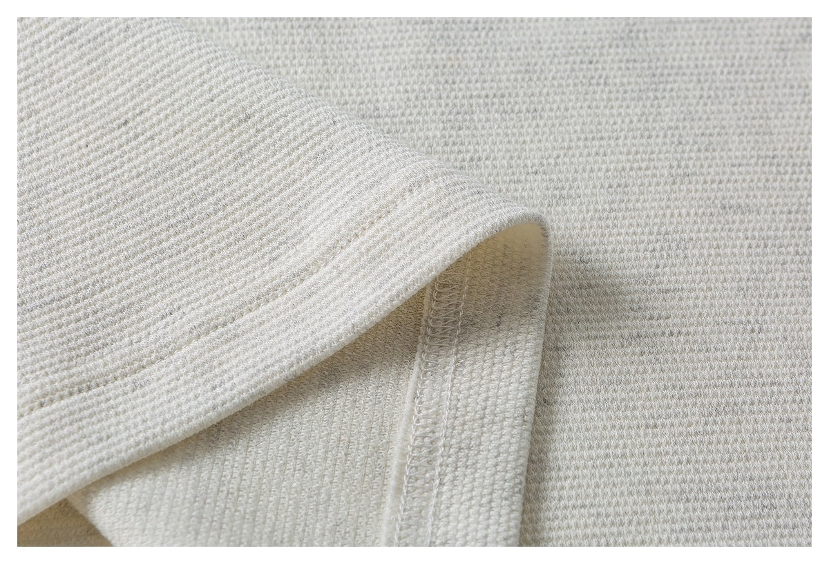 Close-up of the stitched hem and inside seam of an ivory textured top.