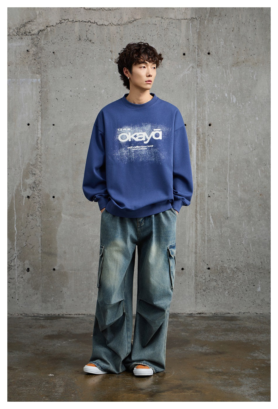 Full-length view of model in a blue graphic sweatshirt with wide-leg faded cargo jeans and sneakers