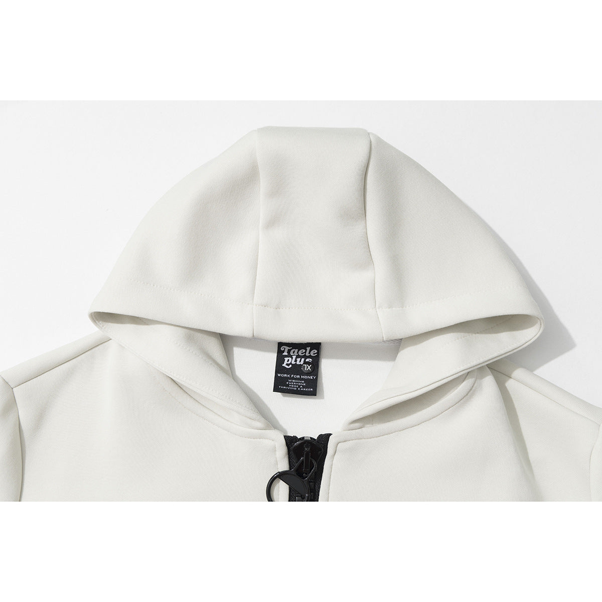 Close-up of an off-white hoodie hood, sewn neck label, and black front zipper pull.