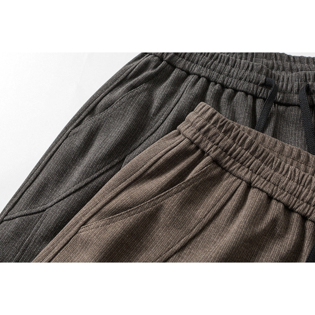 Close-up of brown and charcoal wide-leg trousers showing elastic waistbands, black drawstrings, and textured fabric.