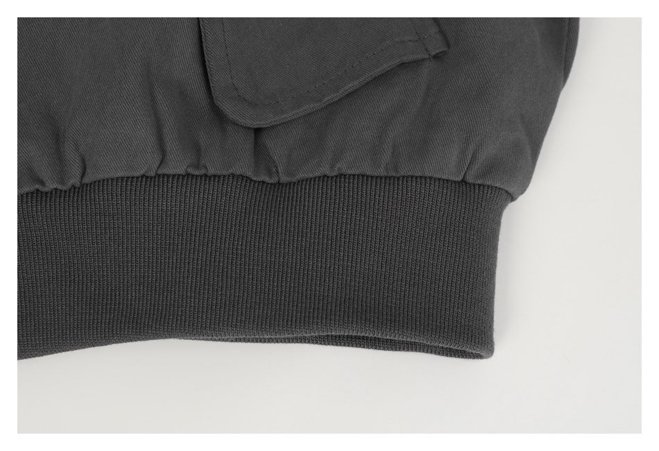 Close-up of a charcoal jacket’s ribbed hem and adjacent flap pocket.