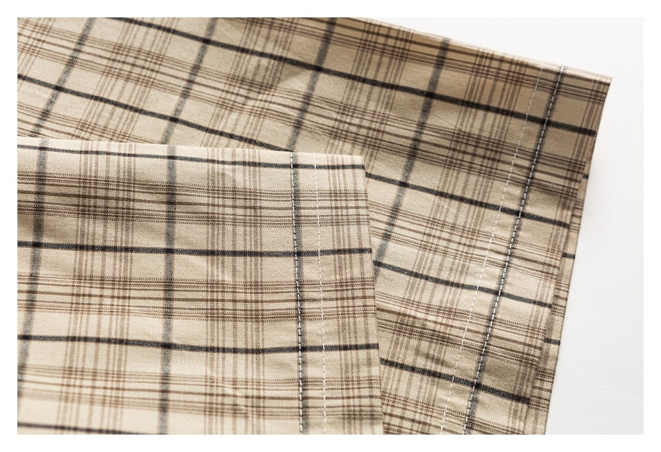 Close-up of beige plaid shirt fabric showing folded edges and parallel stitching.