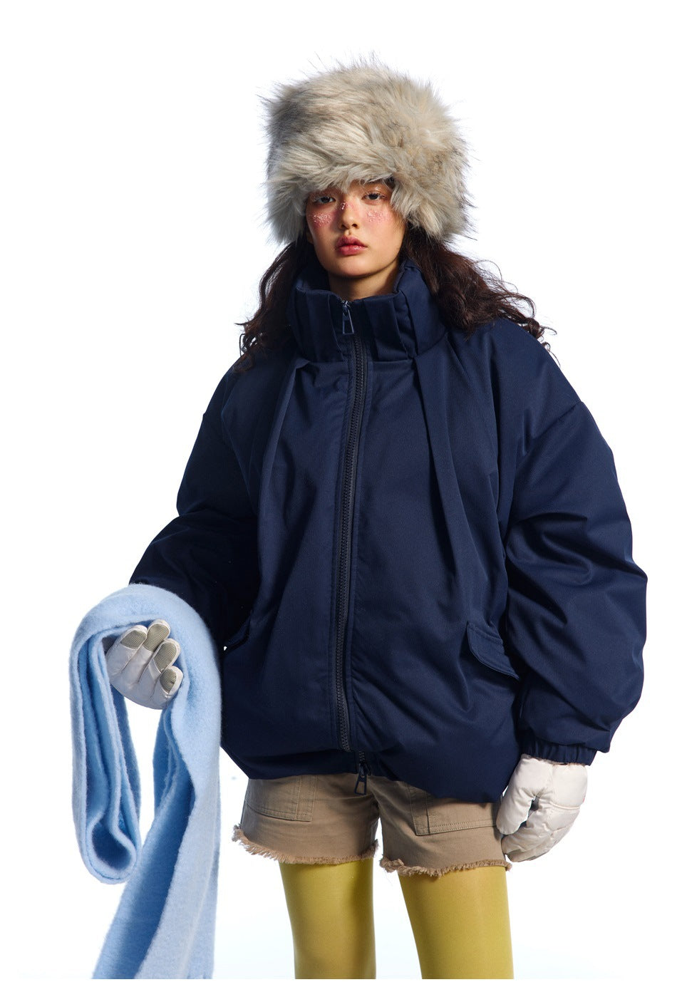 Model wearing an oversized navy zip jacket with a high collar, white gloves, fur hat and pale blue scarf.