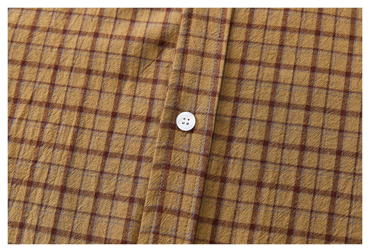 Close-up of a white button and placket on a mustard-brown plaid shirt.