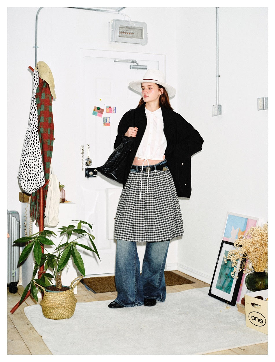 Model in black jacket over a white top, checked skirt and flared jeans, three-quarter view with a black tote bag