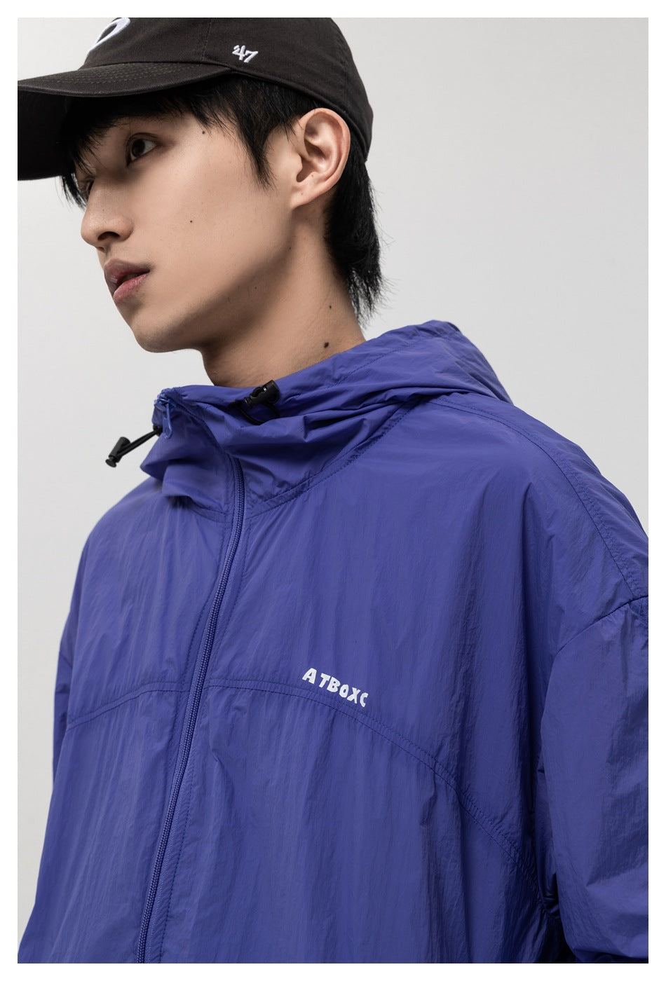 Close-up of a model wearing a blue-purple zip-up hooded jacket with a small white chest mark.
