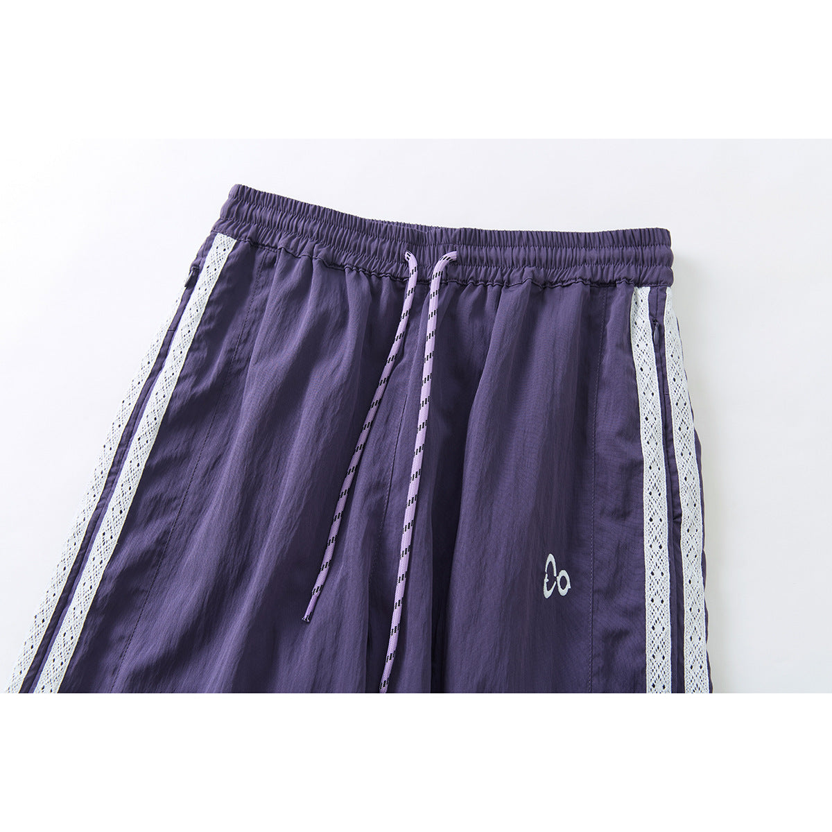 Close-up of purple pants with an elastic drawstring waist, white lace side stripes, and a small emblem.