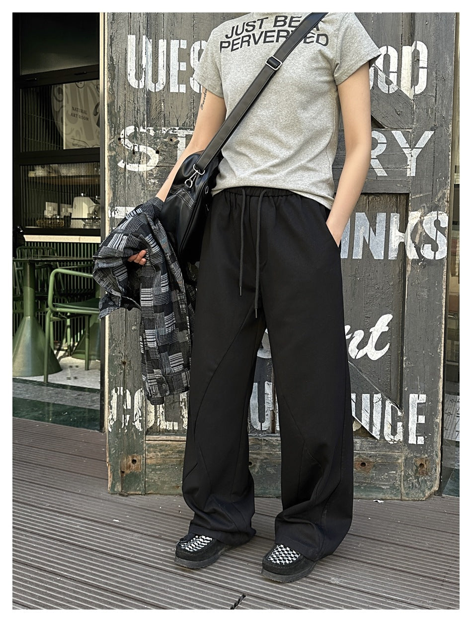 Model wearing black wide-leg drawstring trousers with a gray T-shirt and carrying a patterned overshirt.