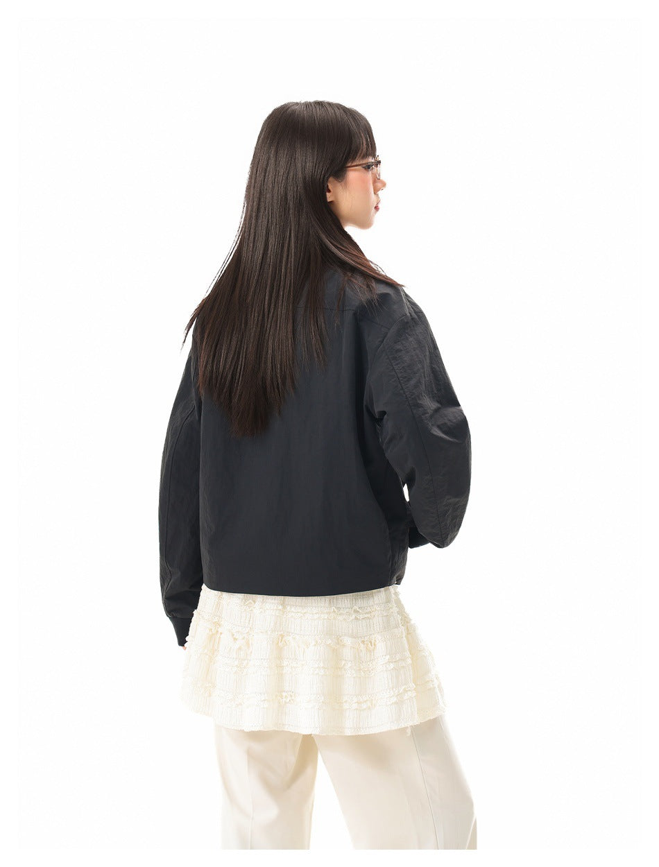 Back view of a model wearing a black long-sleeve jacket with a wide collar, styled over a cream ruffled skirt and trousers.