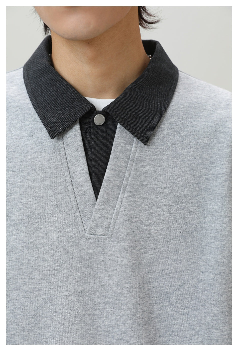 Close-up of a light gray top with a charcoal pointed collar, button, and deep V-shaped placket, worn over a white shirt.