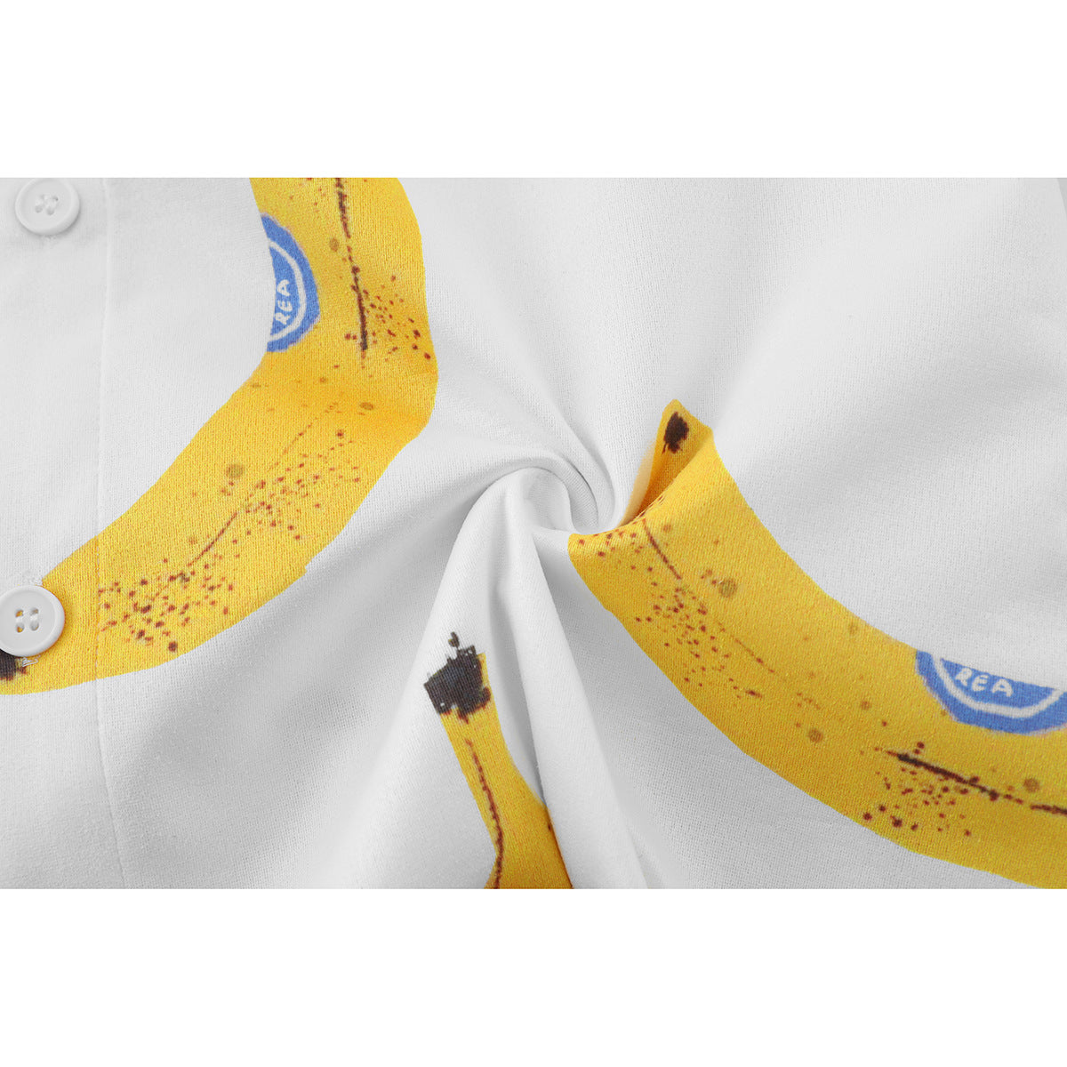 Close-up of white shirt fabric with yellow banana print, white buttons, and a gathered fold.